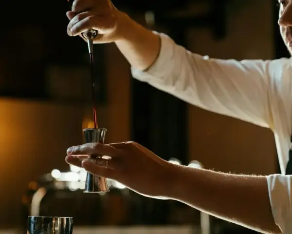 Barman nalewa ciemny płyn do jiggera, przygotowując drinka z Jägermeisterem i sokiem pomarańczowym.