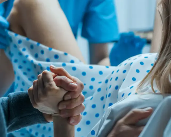 Wsparcie bliskiej osoby podczas porodu. Dłoń partnera trzyma dłoń rodzącej, która ma już widoczny czop śluzowy.