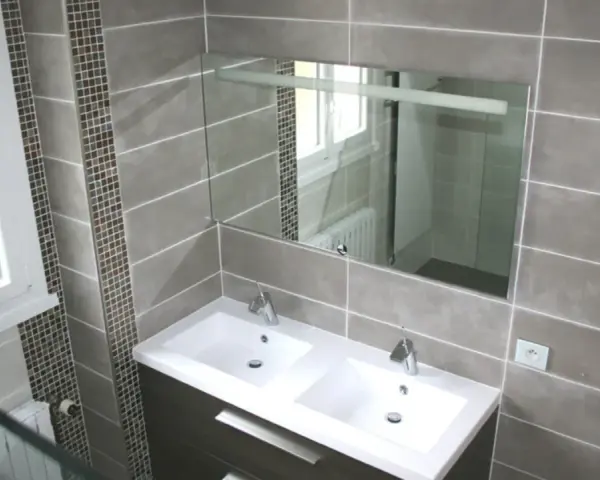 Salle de bain moderne avec double vasque. Le carrelage sol gris, posé au mur, crée une ambiance élégante.