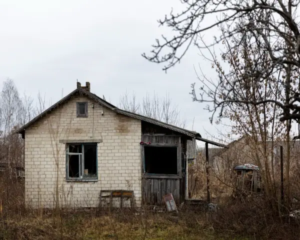 Casa de ladrillo blanco, abandonada, con ventanas rotas y vegetación seca. Un ejemplo de la ley sobre casas abandonadas.