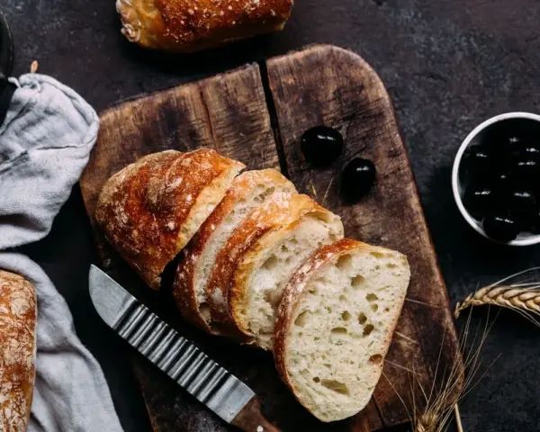 Frisches Brot, aufgeschnitten auf einem Holzbrett, daneben Oliven. Perfekt für den Gasgrill bei richtiger Temperatur.