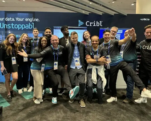 A lively group of Cribl customers and staff pose for a photo at a trade show, all smiles and team spirit.