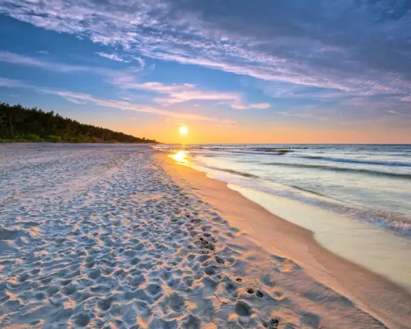 Zachód słońca nad morzem, piaszczysta plaża z ludzkimi śladami, las w tle. Idealne, fajne miejsce nad morzem dla dwojga.