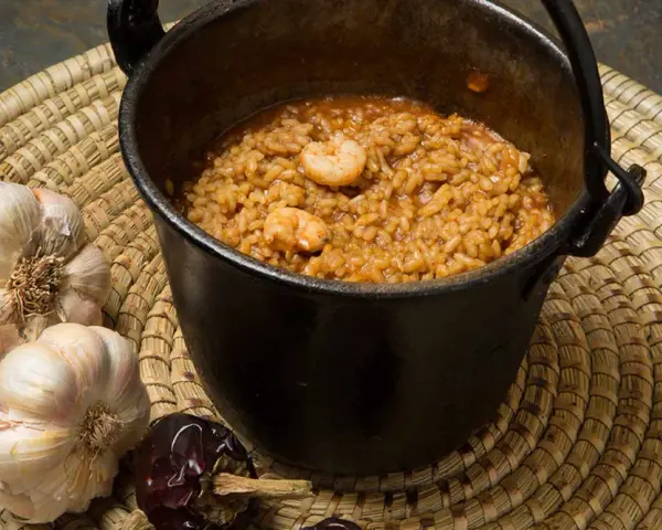 Caldero murciano humeante en olla de hierro, con gambas, ajos y pimientos secos.