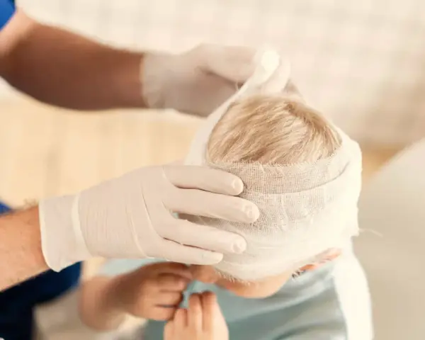 Manos enguantadas vendan la cabeza de un niño, curando sus heridas.