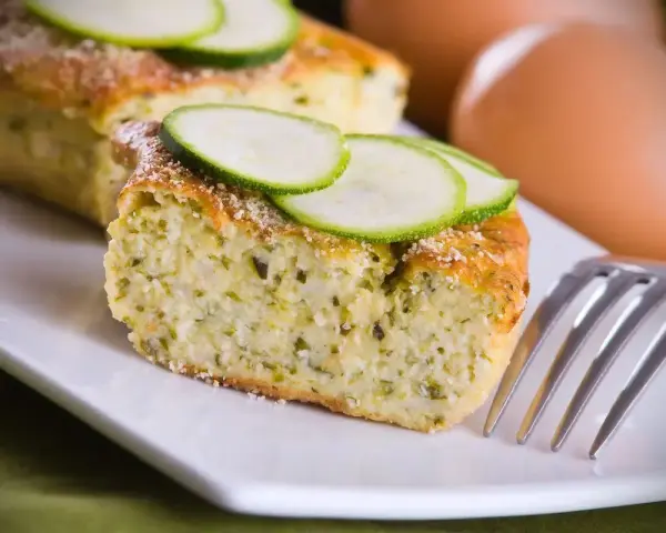 Saporito sformato di zucchine, guarnito con fette di zucchina fresca e una spolverata di parmigiano. Perfetto per un pasto leggero.