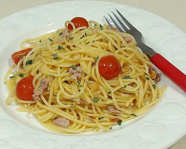 Espaguetis al ajillo con tomates cherry y atún, servidos en plato blanco con tenedor rojo.