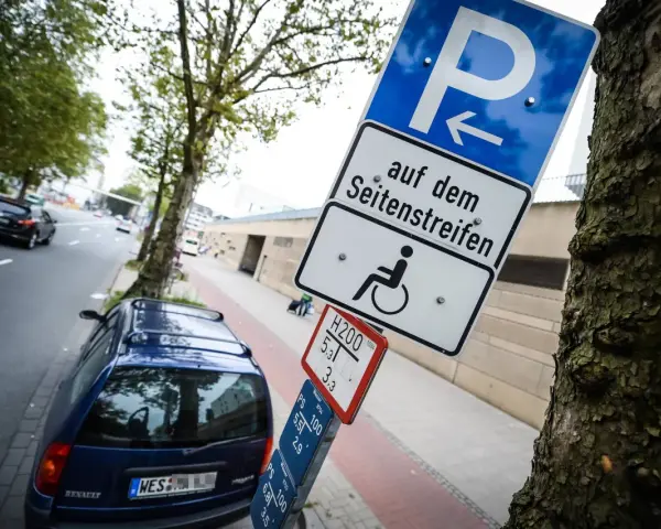 Schild für Behindertenparkplatz auf dem Seitenstreifen. Falschparken wird mit einer hohen Strafe geahndet.