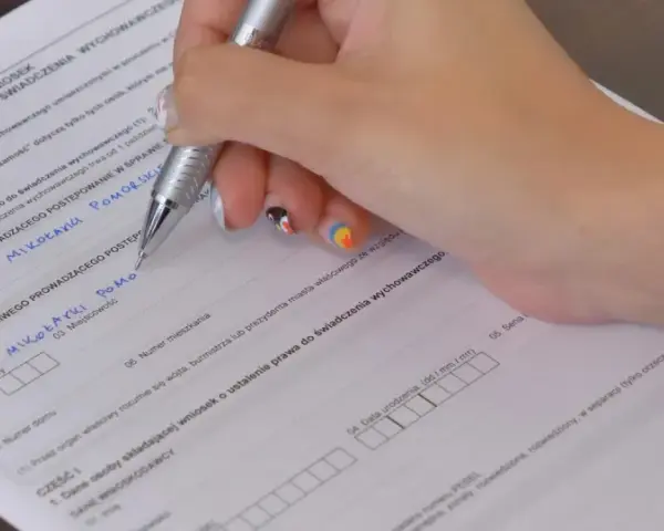 Ręka wypełnia kwestionariusz osobowy, wpisując dane dotyczące świadczenia wychowawczego.