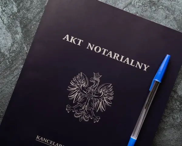 Na ciemnogranatowej okładce widnieje napis "AKT NOTARIALNY" i godło Polski. Obok leży niebieski długopis.