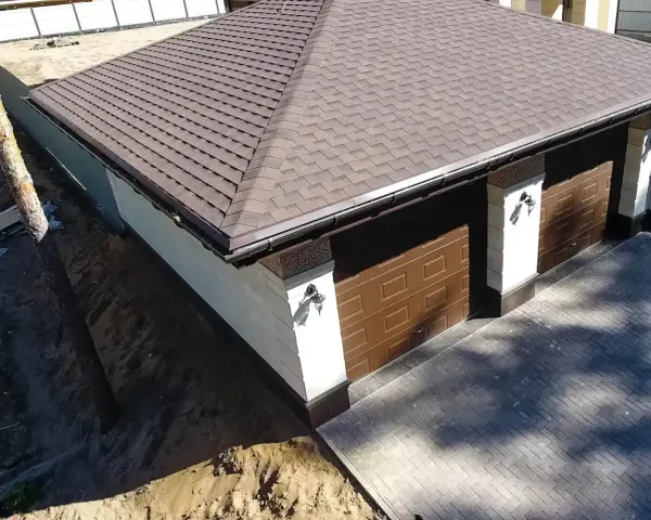 Nowy dach papa na garażu z brązowymi drzwiami i ozdobnymi słupkami.