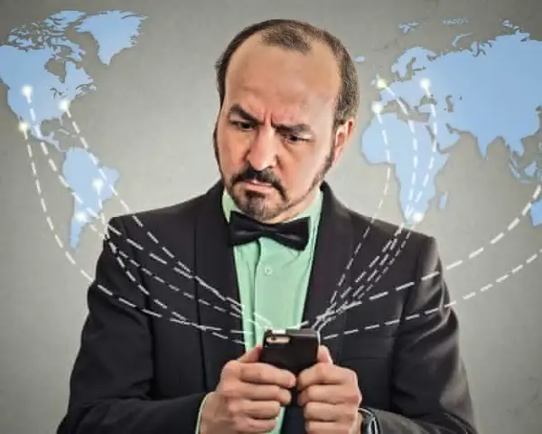 Mężczyzna w garniturze z telefonem, zastanawia się, co to roaming. Mapa świata z połączeniami sugeruje globalną sieć.