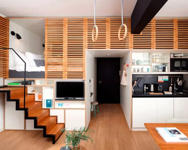 Estudio moderno de piso 25 metros cuadrados con cama elevada, cocina compacta, zona de TV y escaleras de madera.