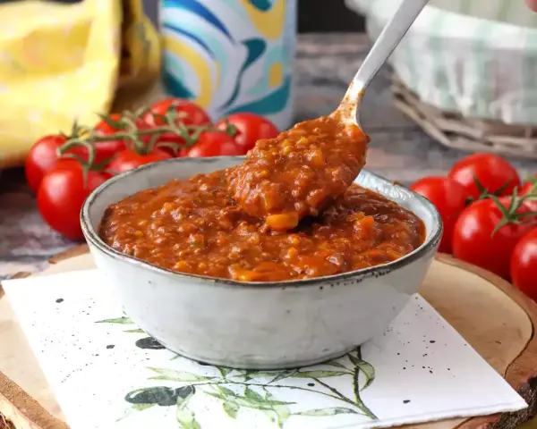 Gęsty, aromatyczny sos bolognese w misce, gotowy do podania. Obok świeże pomidory.