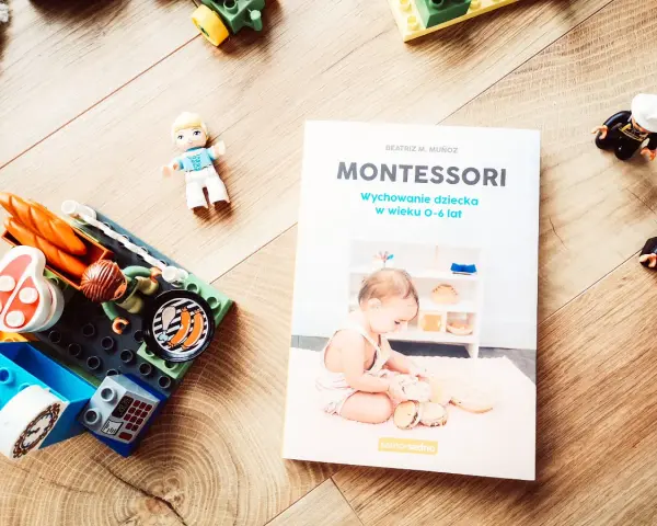 Książka "Montessori. Wychowanie dziecka w wieku 0-6 lat" obok klocków i figurek. Idealna do nauki przez zabawę.