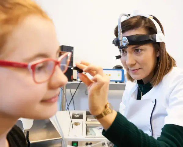 Lekarka bada ucho dziewczynki, która ma okulary. Badanie może pomóc zdiagnozować niedosłuch u dziecka.