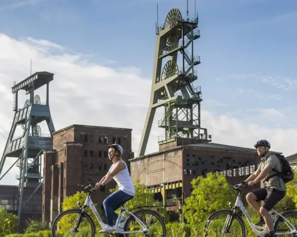 Zwei Radfahrer genießen die Landschaft am ehemaligen Bergwerk Ewald. Die imposanten Fördertürme stehen im Hintergrund.
