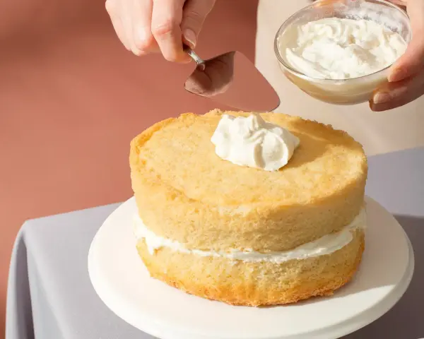 Nakładanie puszystego kremu na biszkoptowe ciasto z mascarpone.