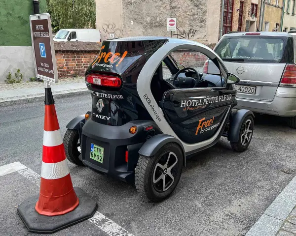 Czarny Renault Twizy z napisem "Free! for our guests" zaparkowany przed hotelem Petite Fleur. Obok znak parkingowy dla gości hotelowych.