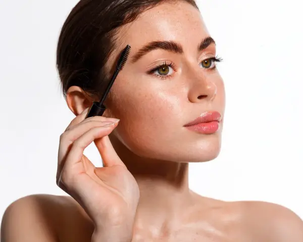 Une femme applique un mascara pour un maquillage des yeux parfait. Ses sourcils sont brossés et ses cils sont mis en valeur.