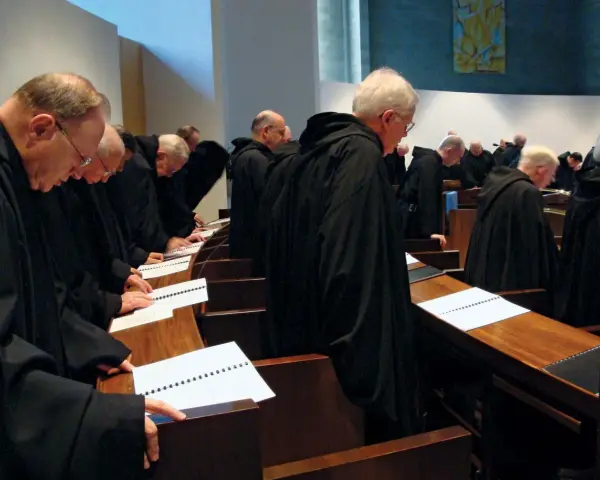 A group of Italian monks in black robes stand in a church, heads bowed over open prayer books.