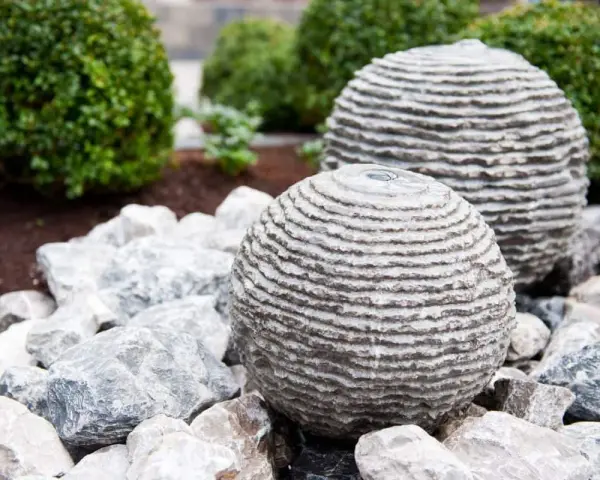 Dwie kamienne kule z betonu, przypominające ułożone krążki, stanowią element wodnej instalacji ogrodowej. Dowiedz się, jak zrobić kulę z betonu.