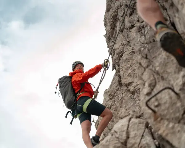 Kletterin im orangefarbenen Anzug sichert sich am Drahtseil des Alpspitz Klettersteigs. Ein spannendes Abenteuer in den Bergen.