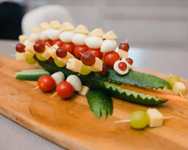 Krokodil aus Gurke mit herzhaftem Fingerfood für Kinder: Käse, Tomaten, Mozzarella & Trauben auf Spießen.