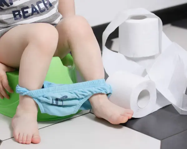 Dziecko na nocniku, z opuszczonymi majtkami, obok rolki papieru toaletowego. Wygląda na to, że pojawiła się biegunka u dziecka bez innych objawów.
