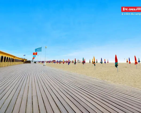 Plage de Deauville, parfaite pour une vacance scolaire en Normandie. Cabines colorées, parasols et ciel bleu azur.