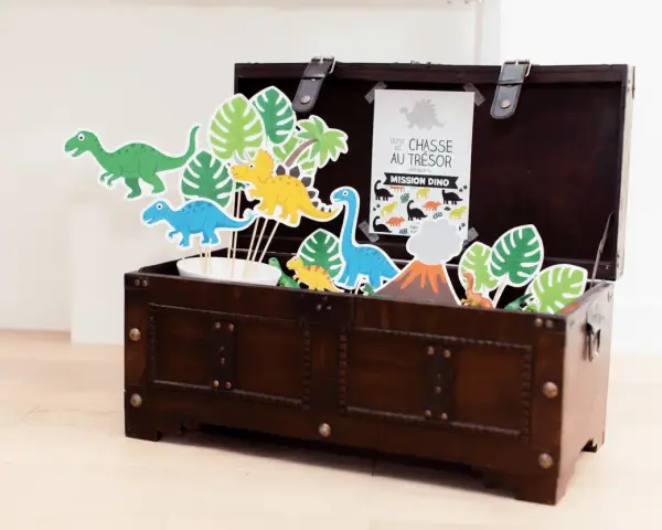 Coffre en bois rempli de décorations de dinosaures et de feuilles tropicales.