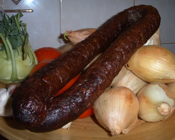 Wędzona kiełbasa z dzika na talerzu z warzywami: cebulą, pomidorami, kalarepą i czosnkiem.