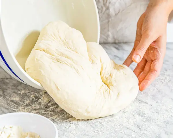 Frischer Teig, der aus einer Schüssel auf eine bemehlte Arbeitsfläche gleitet. Ähnlich wie Mehl Typ 0, ideal zum Backen.