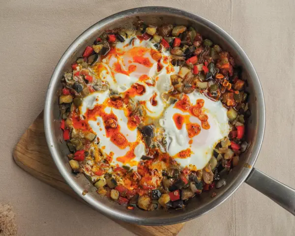 Huevos al plato con verduras salteadas, pimientos, calabacín y berenjena, todo en una sartén.