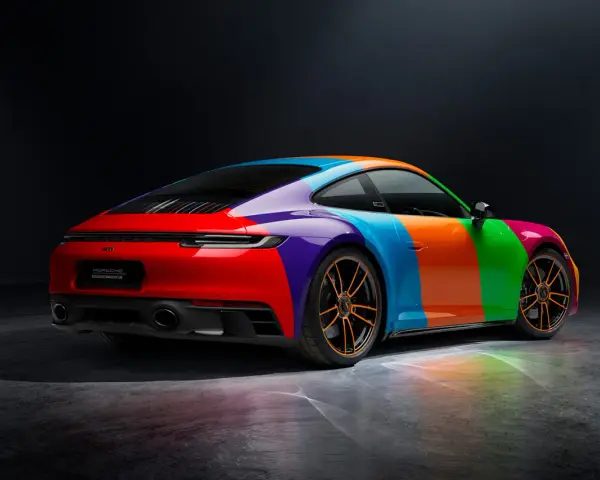 Porsche 911 Carrera GTS w tęczowym malowaniu, z pomarańczowymi felgami i odbiciami światła na podłożu.