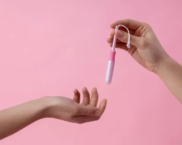 Dwie dłonie, jedna trzyma tampon z aplikatorem, druga wyciągnięta do przyjęcia. Ciasna pochwa to temat, który wymaga dyskrecji.