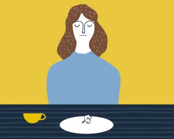 Una donna con gli occhi chiusi è seduta a tavola, davanti a una tazza e un piatto con un piccolo cibo. Un promemoria su cosa non dire a chi soffre di disturbi alimentari.
