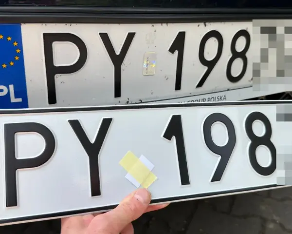 Dwie polskie tablice rejestracyjne PY 198. Jedna jest zamontowana na samochodzie, druga trzymana w ręku.