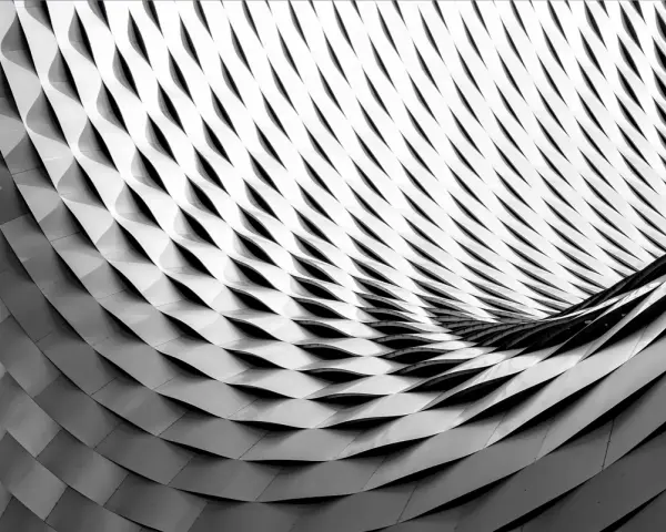 Composition d'image abstraite en noir et blanc, montrant une structure métallique aux formes ondulées et répétitives, créant un jeu d'ombres et de lumières.