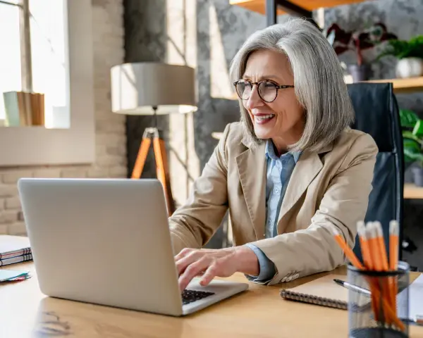 Femme souriante travaillant sur son ordinateur portable, planifiant sa future pension pré cheval.