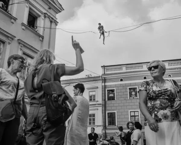 Street foto: tłum na ulicy obserwuje śmiałka balansującego na linie.