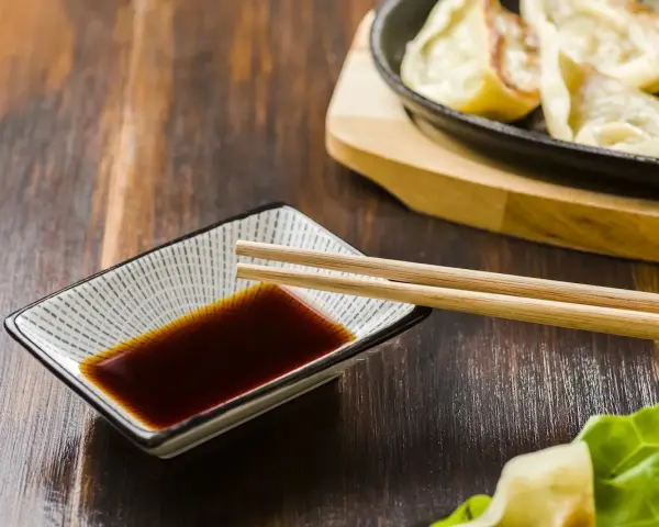 Sos sojowy w miseczce z pałeczkami, obok pierożków gyoza. Szukasz alternatywy, czym zastąpić sos sojowy?