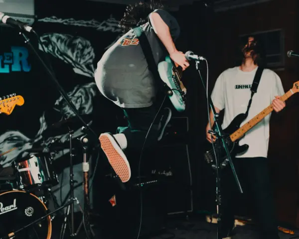 Ein Gitarrist springt auf der Bühne, während ein Bassist spielt. Das ist Rockmusik in Aktion!