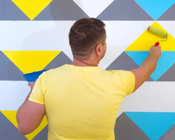 Un homme peint un mur avec un rouleau, créant un modèle de peinture géométrique aux couleurs vives.