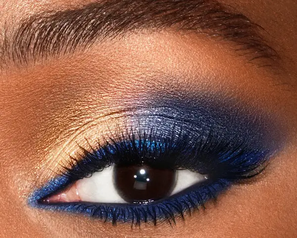 Un œil aux smoky eyes bleus intenses, rehaussé de fard doré et de paillettes. Un regard captivant.