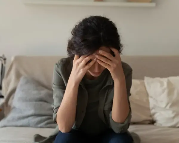 A woman sits with her head in her hands, overwhelmed by the cycle of self-destruction.
