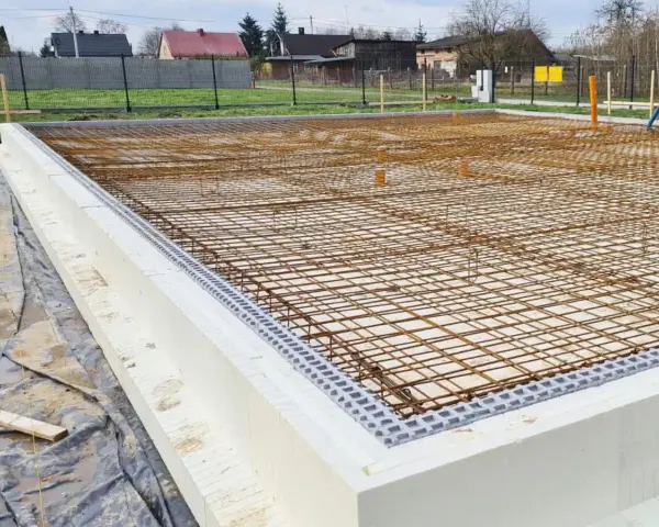Siatka zbrojenia na fundamencie z białych bloczków styropianowych, gotowa do zalania betonem.