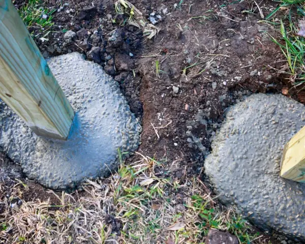 Holzpfosten werden in frisch gegossenen Beton gesetzt, um einen stabilen Zaun zu bauen. Das Einbetonieren der Zaunpfosten sorgt für Langlebigkeit.