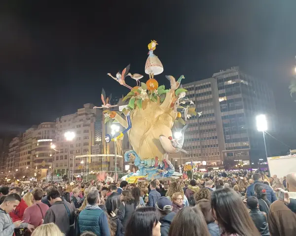 La foule admire une immense sculpture colorée, une scène typique du déroulement des Fallas de Valencia, avec des flamants roses et une petite fille perchée en haut.