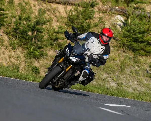 Motocyklista w kasku na zakręcie górskiej drogi. Planujesz podróż na Korsykę? Sprawdź ceny paliwa i noclegów!